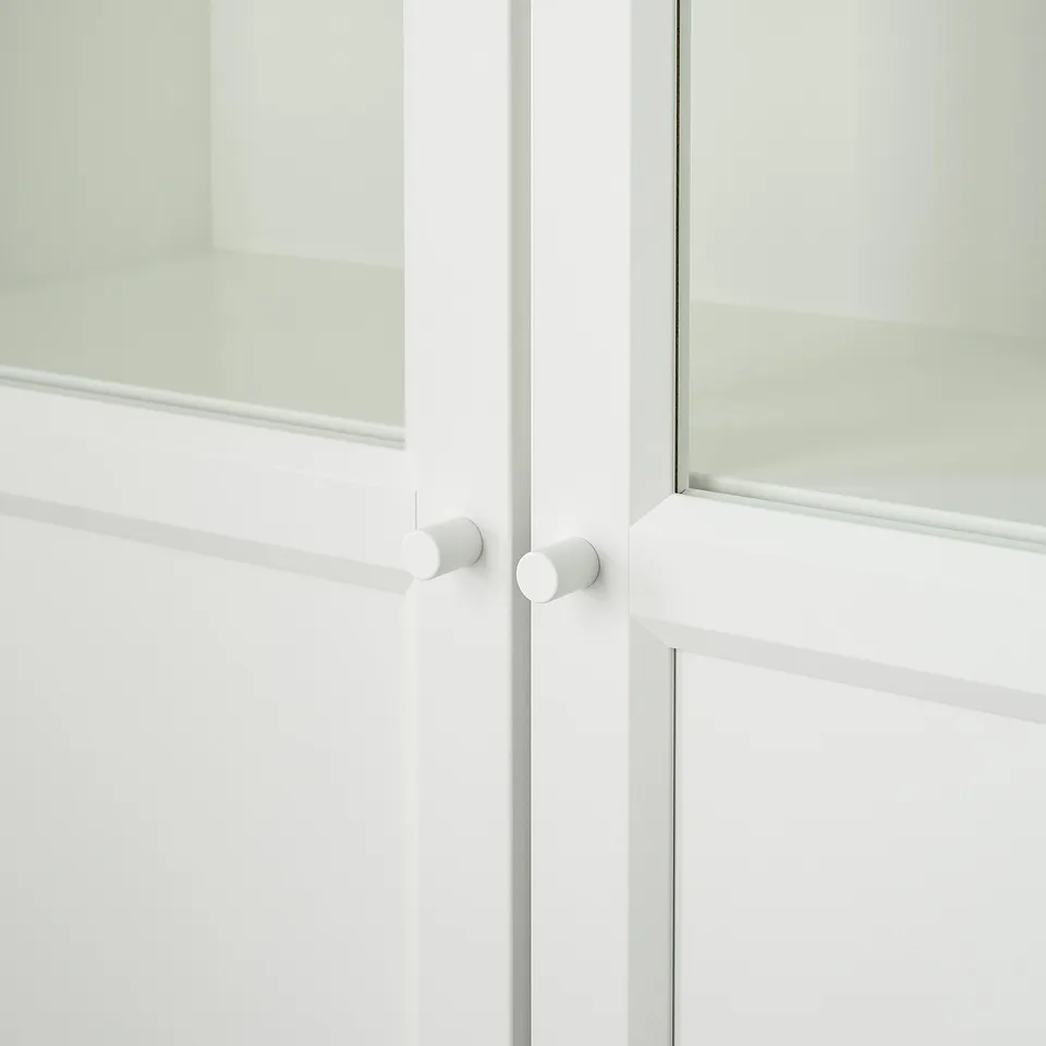 Close-up of white cabinet doors with adjustable hinges, frosted glass panel, and small circular metal handles.