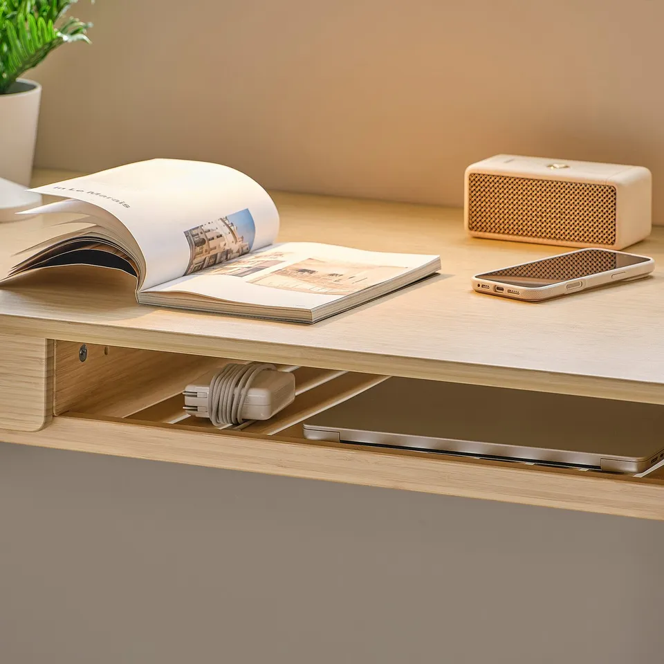 Open magazine on a wooden desk, a smartphone, and a compact speaker beside a neatly organised drawer.