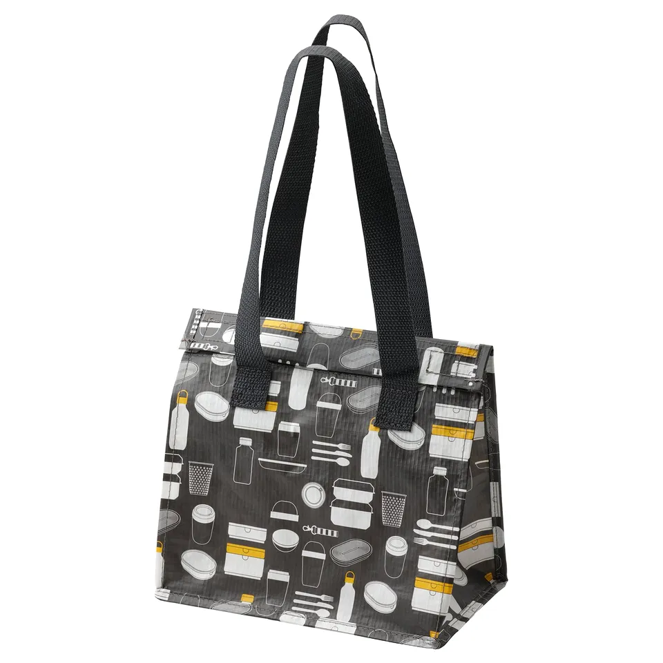 A FLADDRIG lunch bag, black with grey and yellow prints of lunch items. It has sturdy handles for easy carrying.