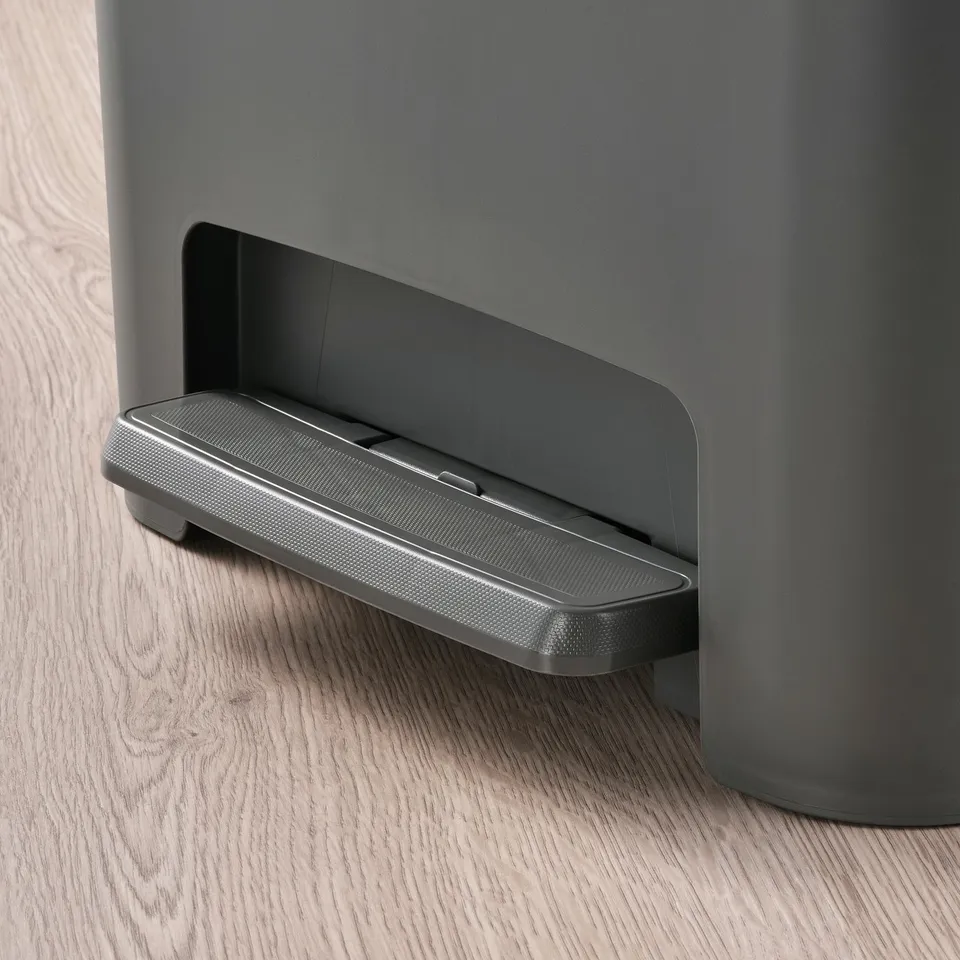 Grey pedal bin with foot pedal, hands-free, stable on wood floor.