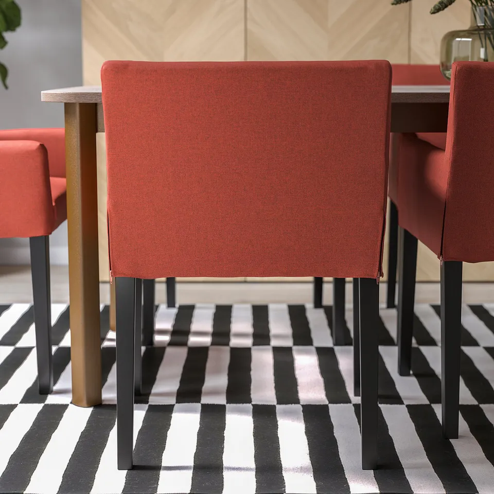 Three red, upholstered dining chairs with black metal legs on a black and white chequered floor.