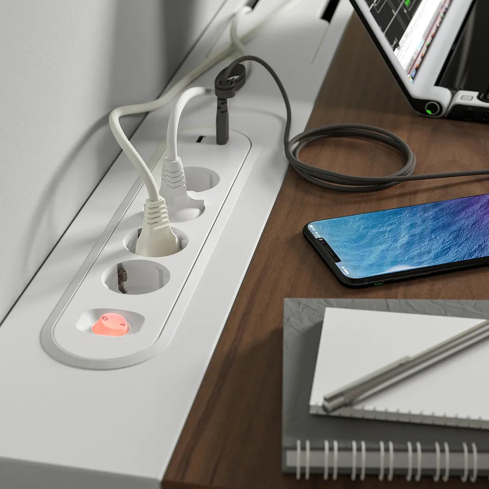 Desk with built-in power sockets and cable management tray. A notebook, phone, and earphones are on it.