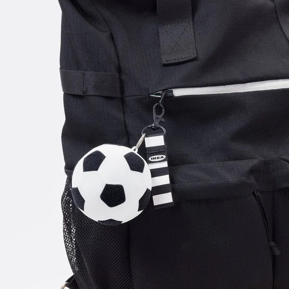 Mini football keychain attached to a black backpack. Football keychain functions as a soft toy or bag accessory.
