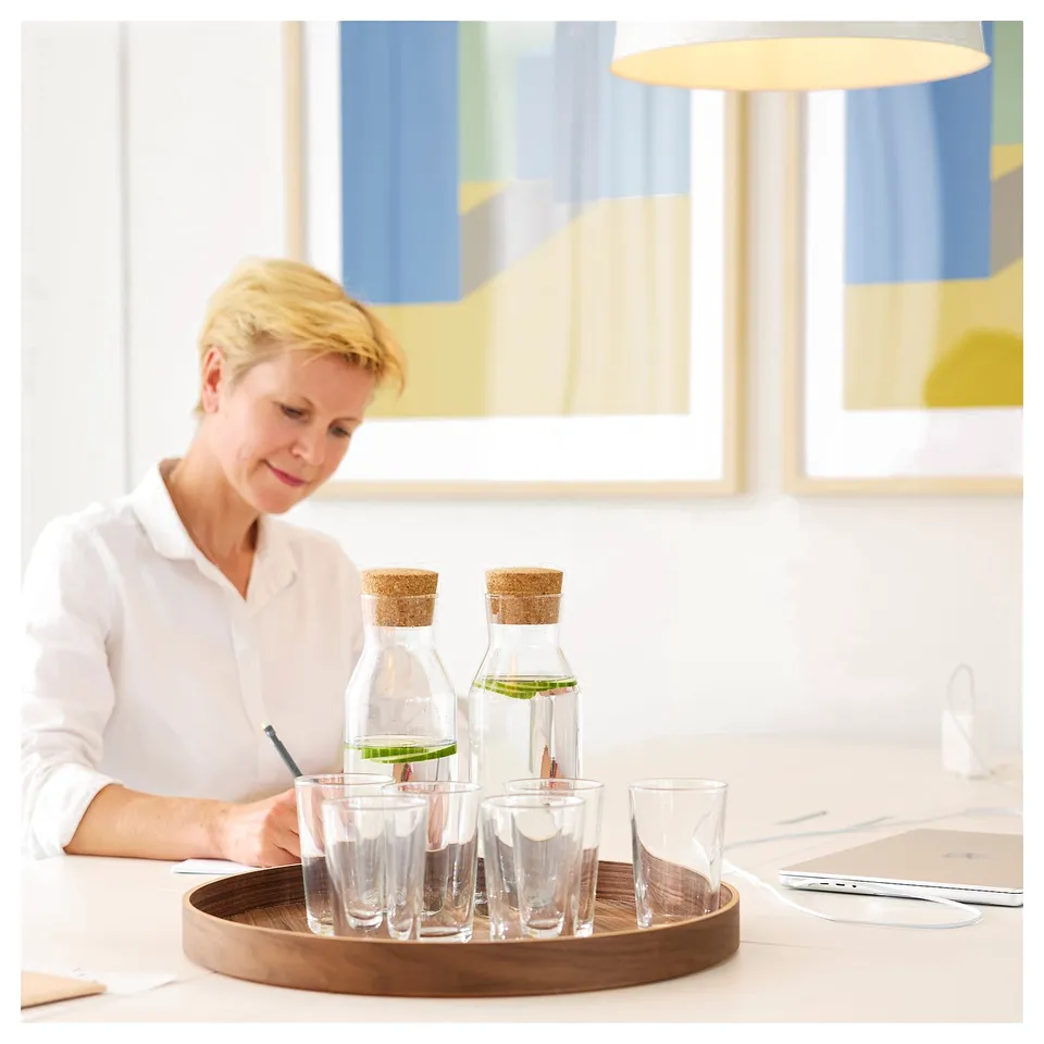 Person at table with water bottles, glasses, laptop, and papers.