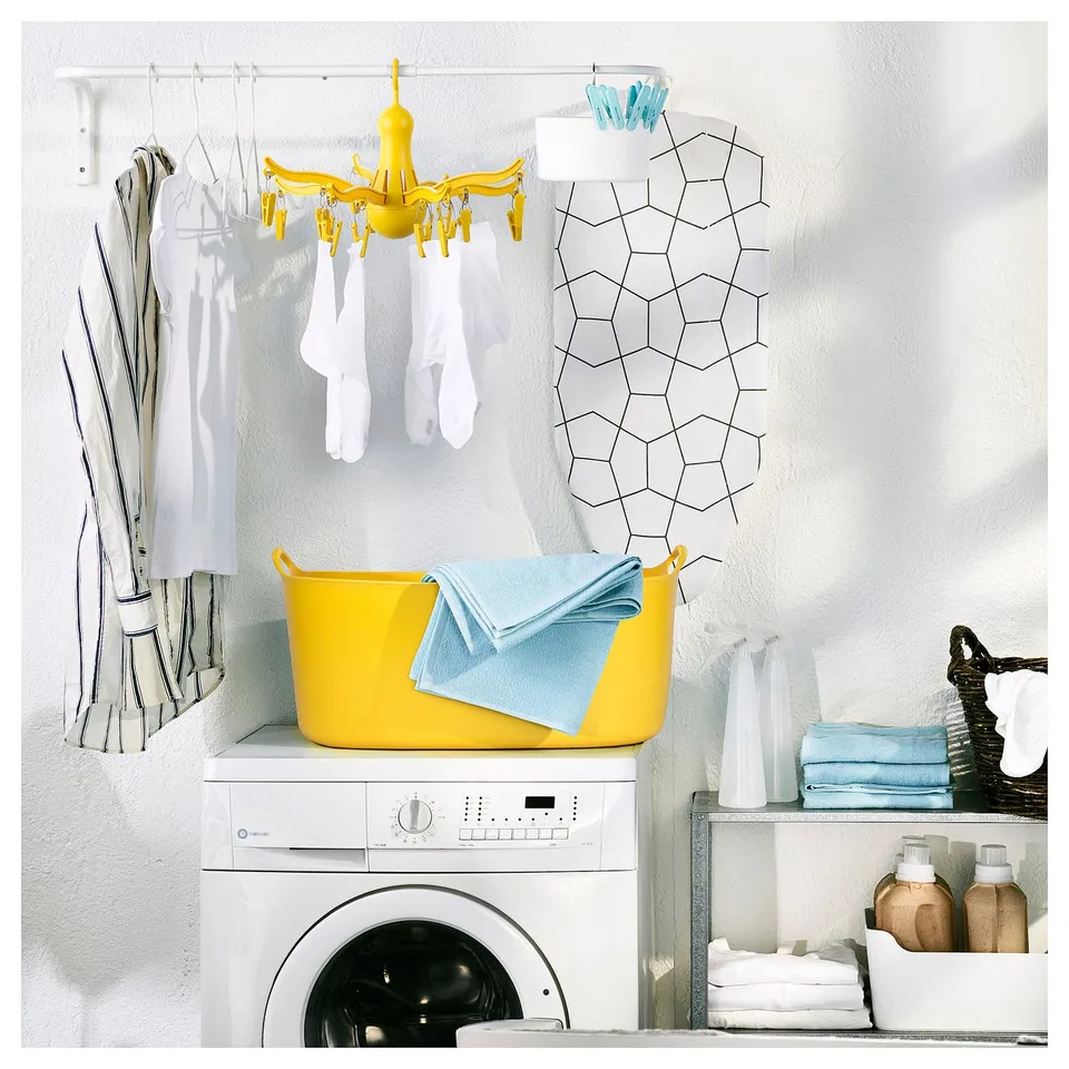 Bright yellow laundry drying rack on wall over washer, holding small clothes and socks.