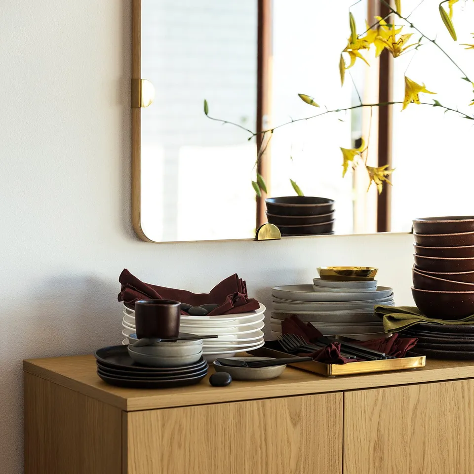 Table setup with plates, cups, bowls on wooden cabinet, mirror, plants.