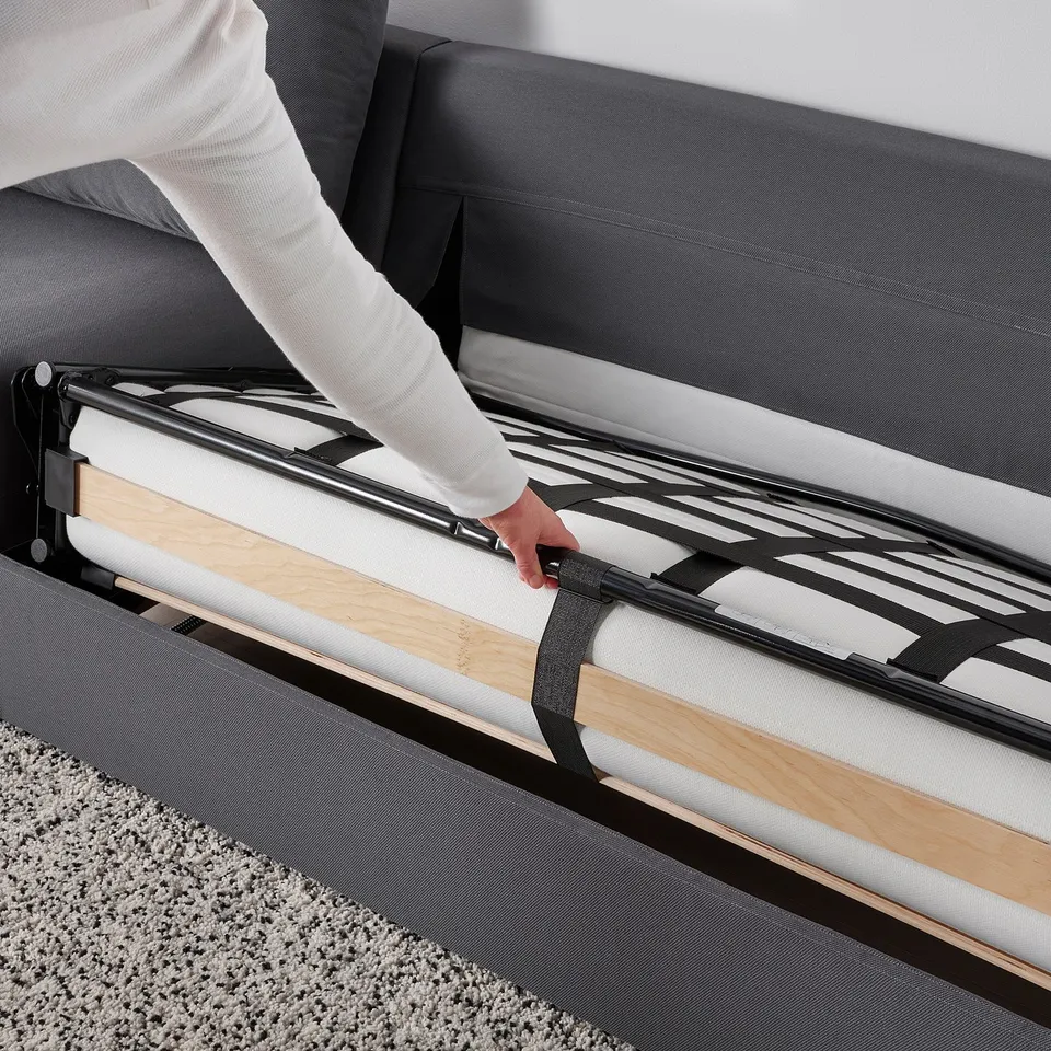Person pulls out sofa-bed, revealing thick mattress on metal slats. Sueitable for comfortable sleeping.