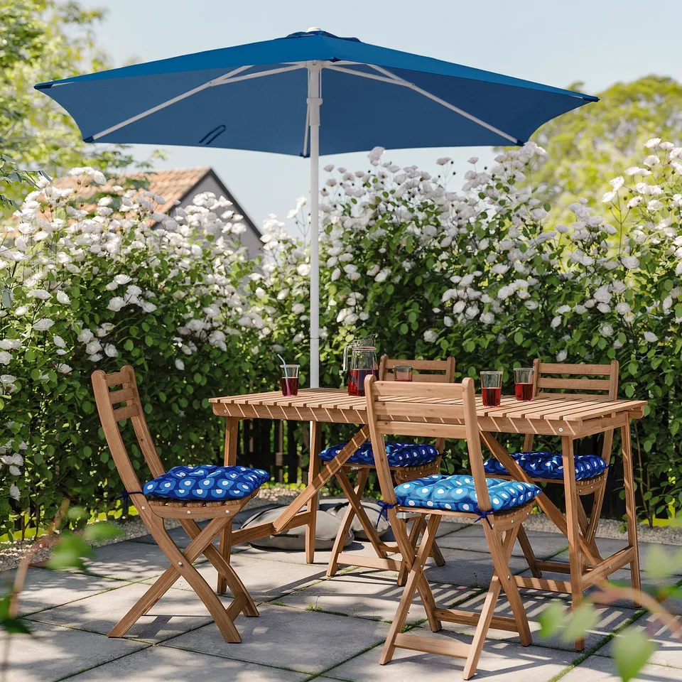 Blue patio set with folding wooden chairs, cushions, and a matching umbrella on a tiled patio.