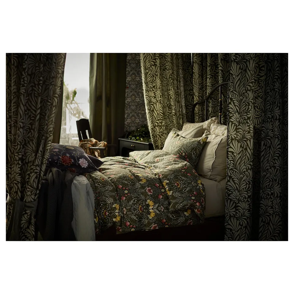 Bedroom with floral patterned bedding in earthy tones, framed by ornate curtains with a matching design, creating a cosy, artistic atmosphere.