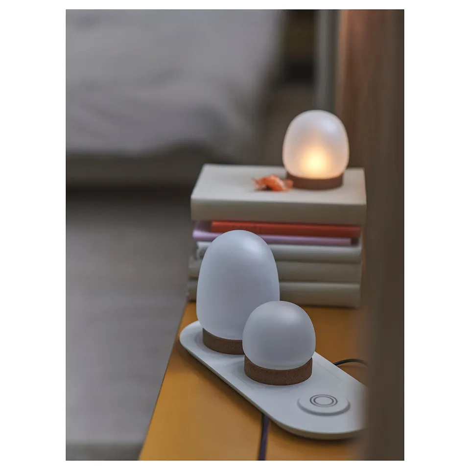 PRAKTSPIREA lamps: 3 white, flickering battery-operated lights on charger, atop books.