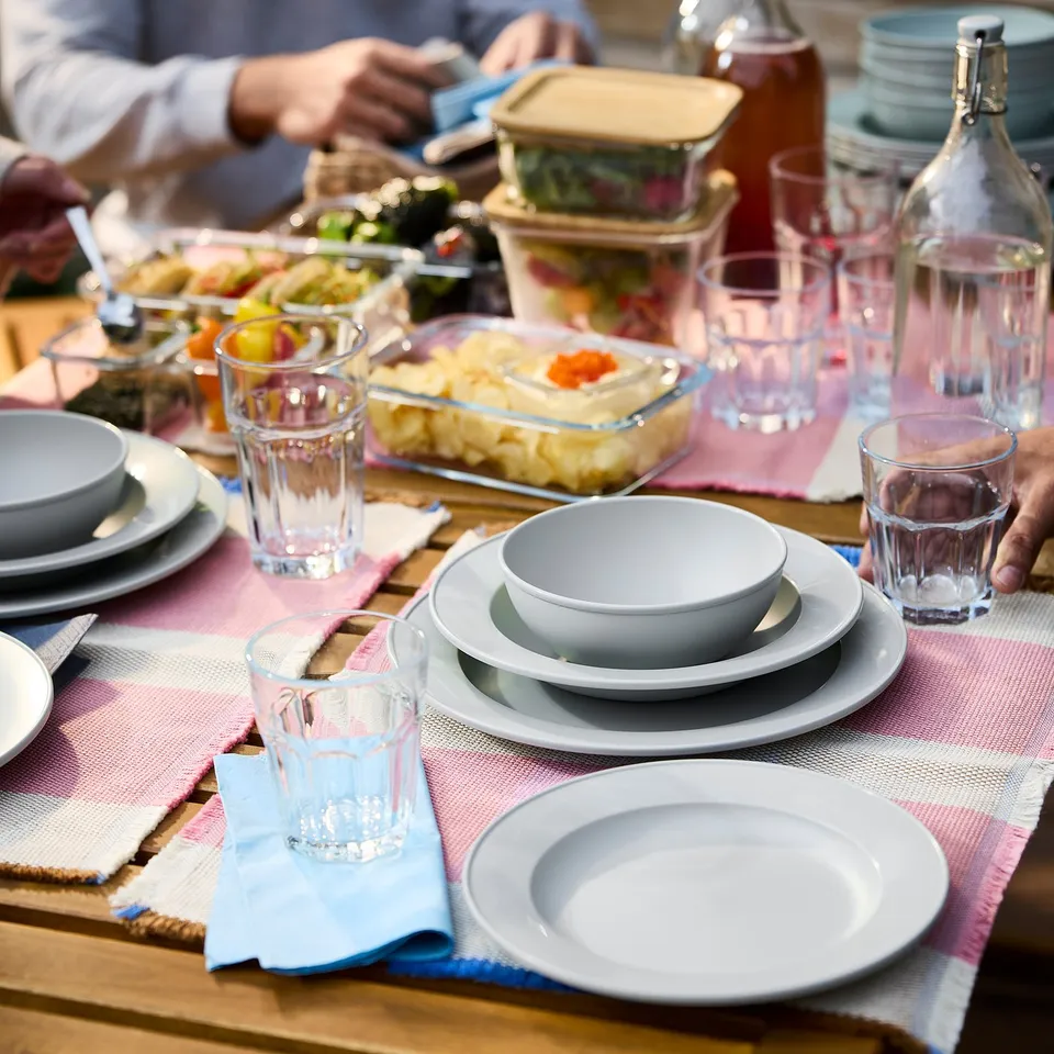 Table set with SIMKRABBA plates in green-grey, glass cups, and various food dishes. Plates are sturdy, simple, and classic with reinforced edges.
