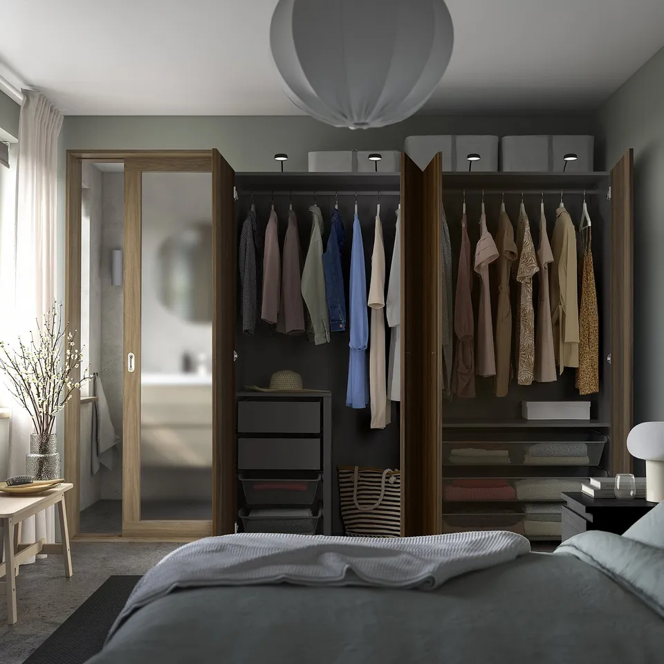 Bedroom with open wardrobe showing clothes, a hat, and storage boxes inside, next to a bed with grey bedding.