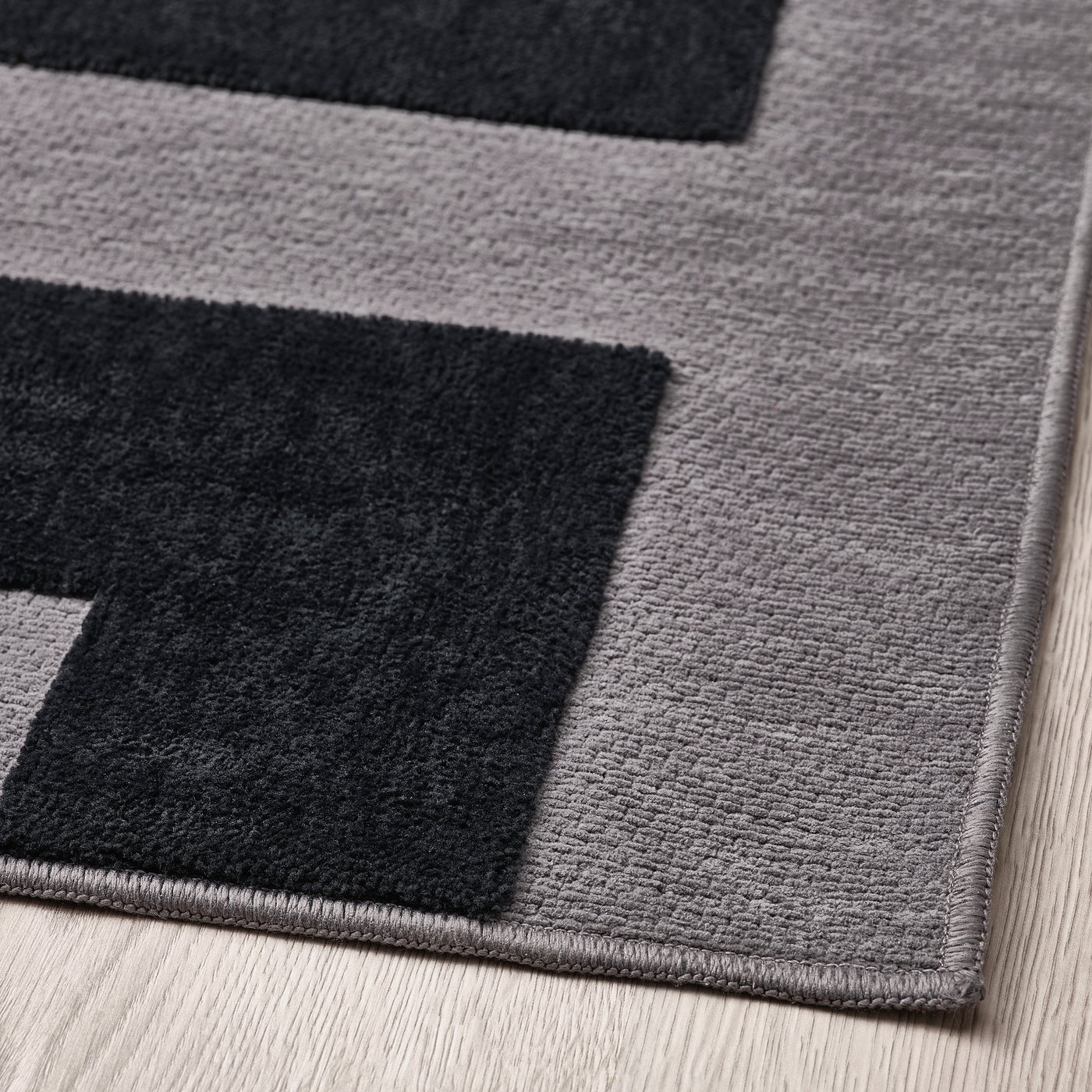 Black and grey rug with geometric pattern, soft texture, folded on light wooden floor.