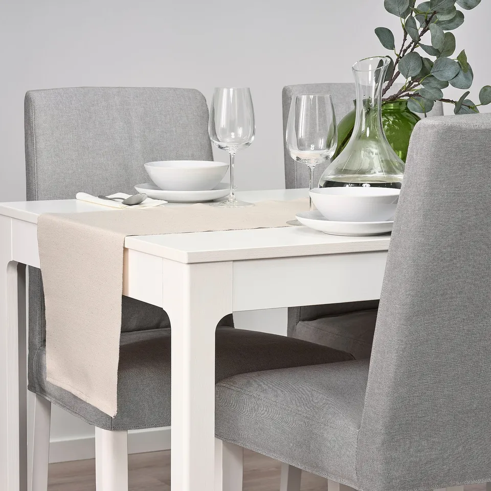 Table set with white dishes, glasses, and pitcher; grey chairs and beige table runner.