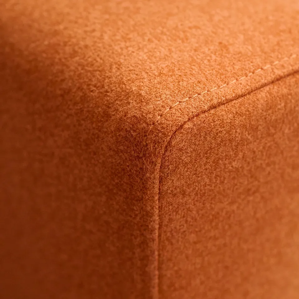 Close-up of an orange, upholstered cushion with visible stitching, showcasing high-quality fabric and craftsmanship.