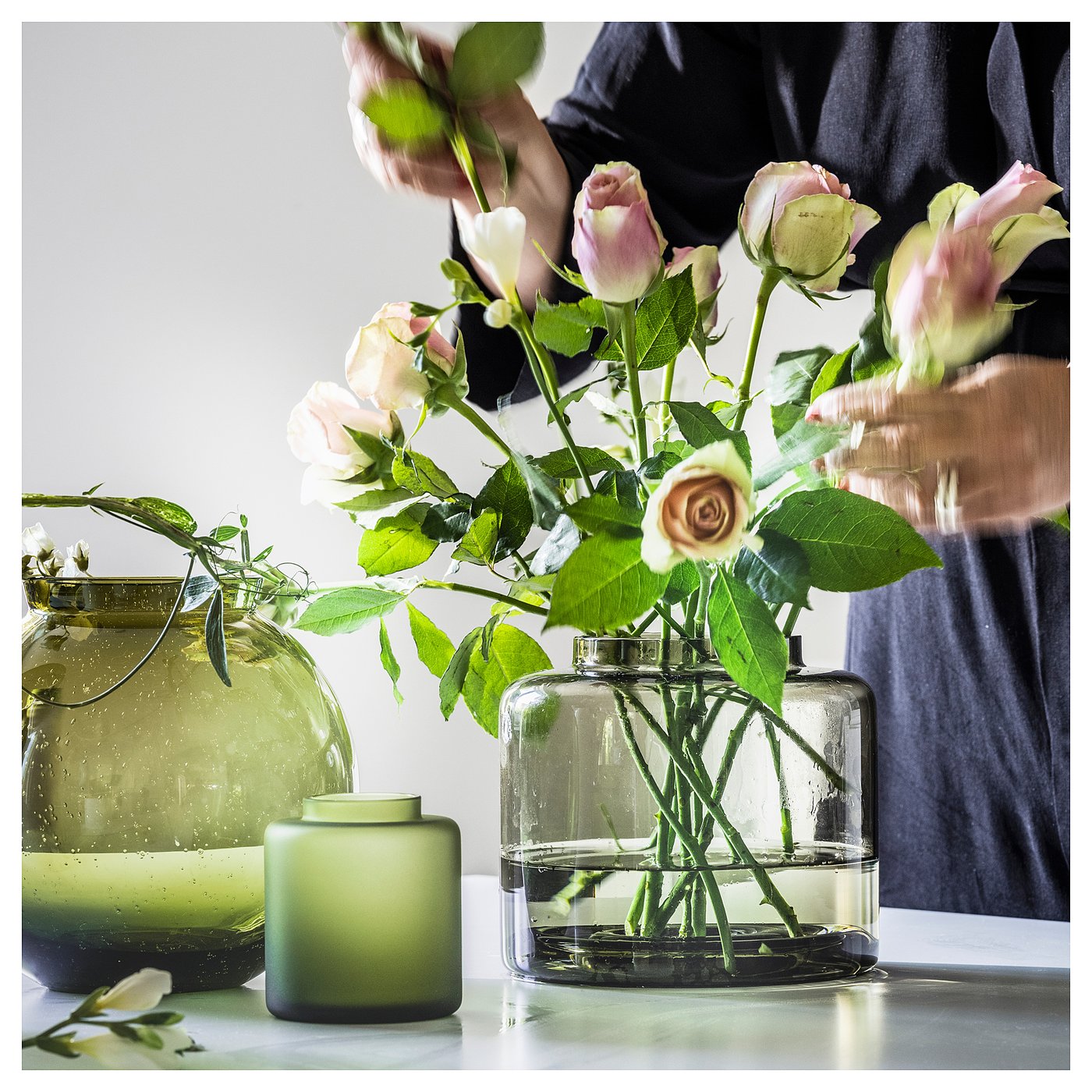 Three vases, one with flowers. Front vase is clear, holds roses. Others are green, one with water droplets. On table.