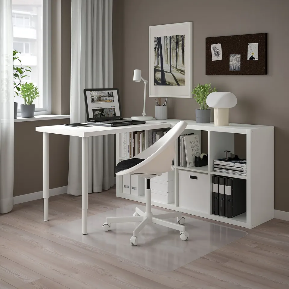 Home office with KALLAX desk, laptop, lamp, books, decor, white chair, large window.
