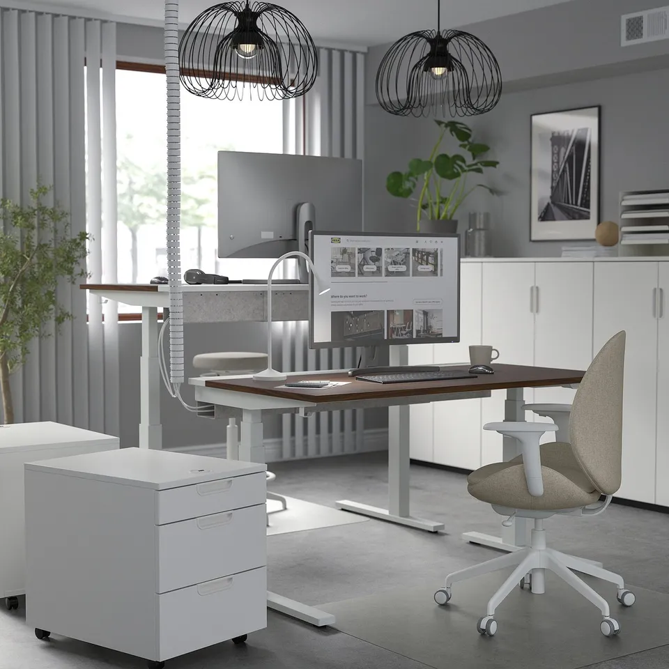 Modern office with MITTZON sit-stand desk, white, ergonomic chair, dual monitor setup, grey walls, large window, and artistic lighting.