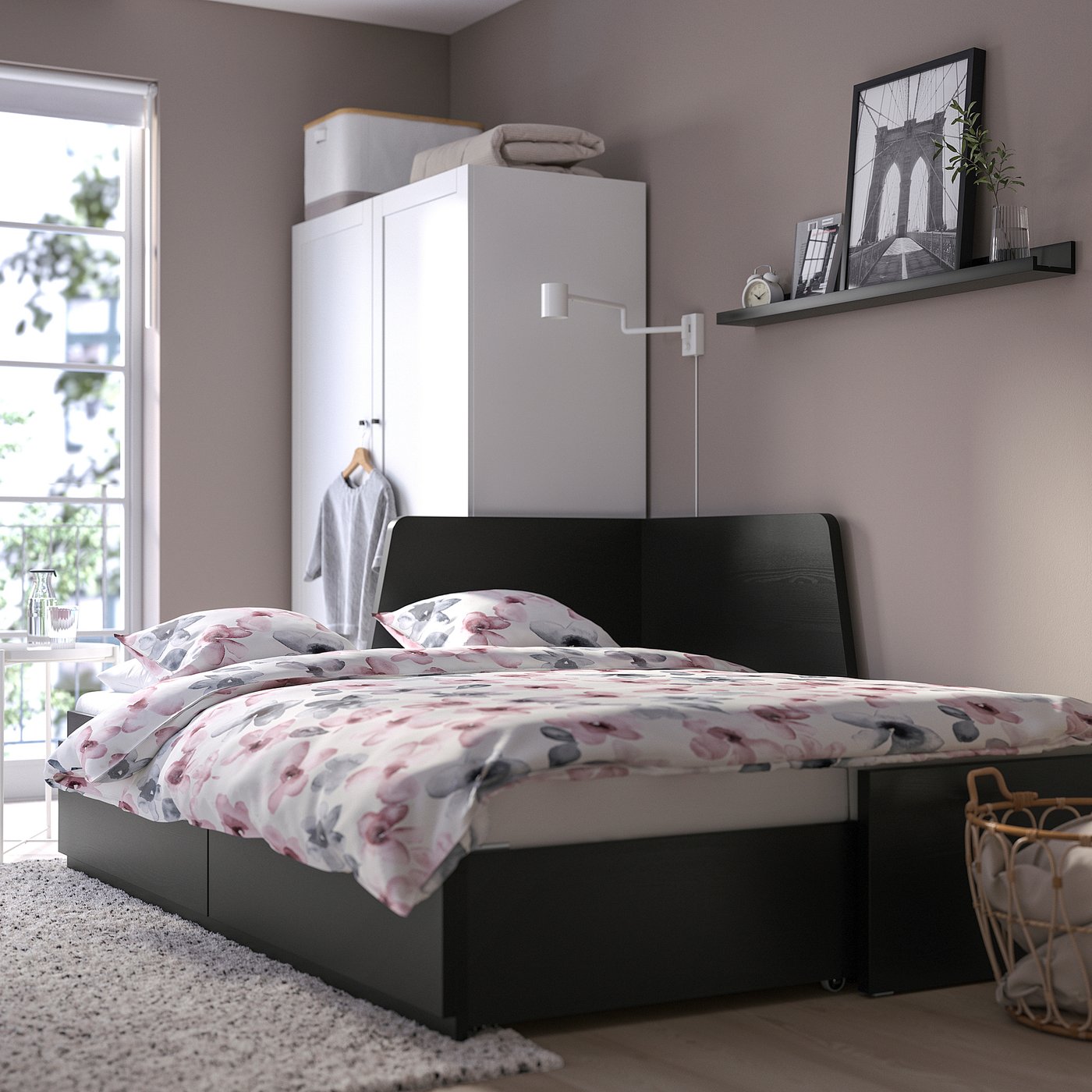 Modern bedroom with a FLEKKE sofa-bed against a wall. The bed floral bedding and drawers. To the right is a shelf with decor.