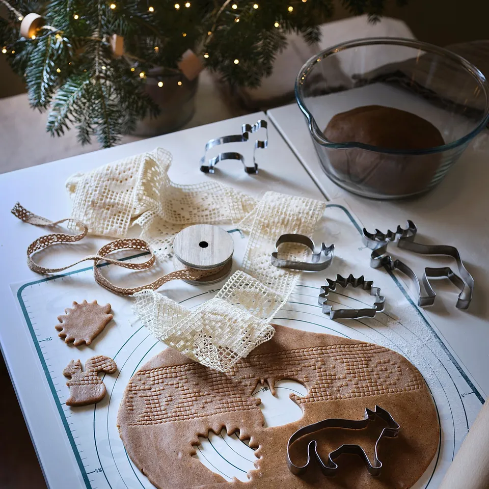 Baking setup with gingerbread dough on mat, cookie cutters, ribbon, and rolling pin. Festive, diy holiday scene.