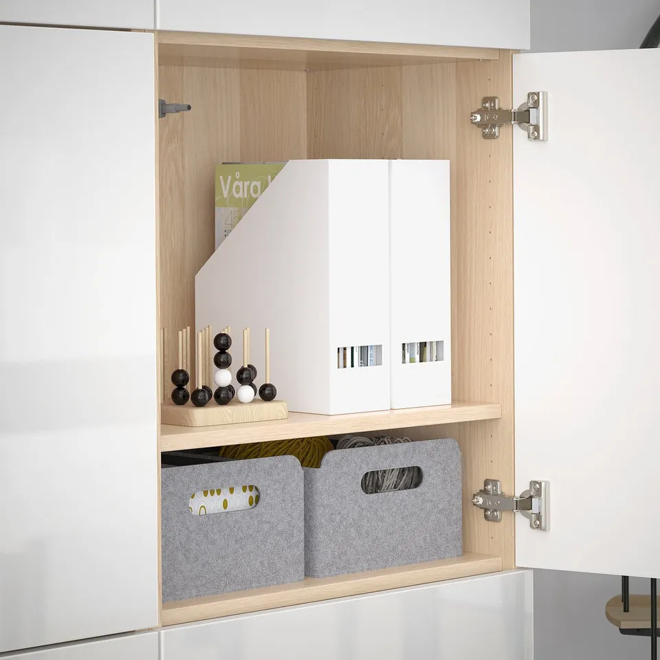 A modern cabinet with two shelves holding decorative spheres, a magazine file, and two grey bins with handles.