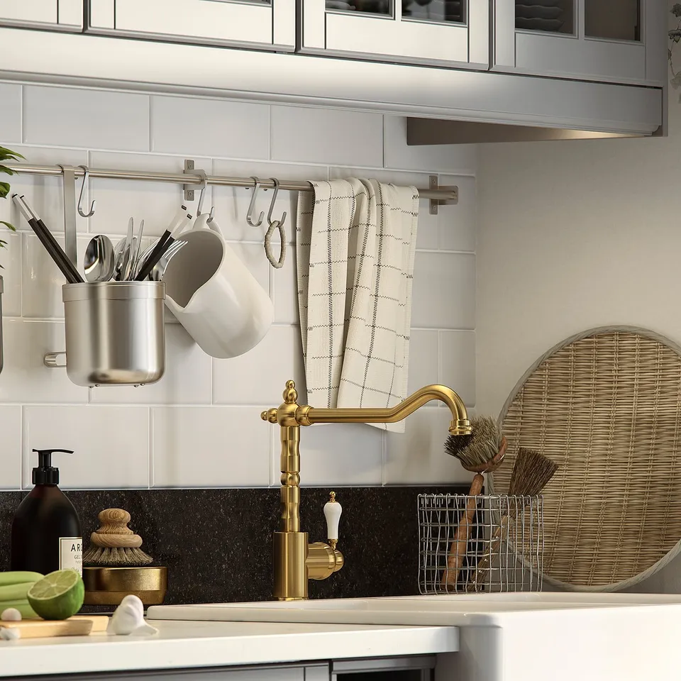 Modern kitchen sink with gold GLITTRAN tap, white countertop, black backsplash, lined towels, and wicker organisers.