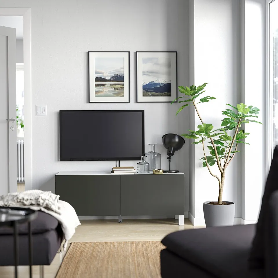 Modern living room with dark grey BESTÅ tv unit, flat-screen tv, framed photos, potted plant, and cosy seating.