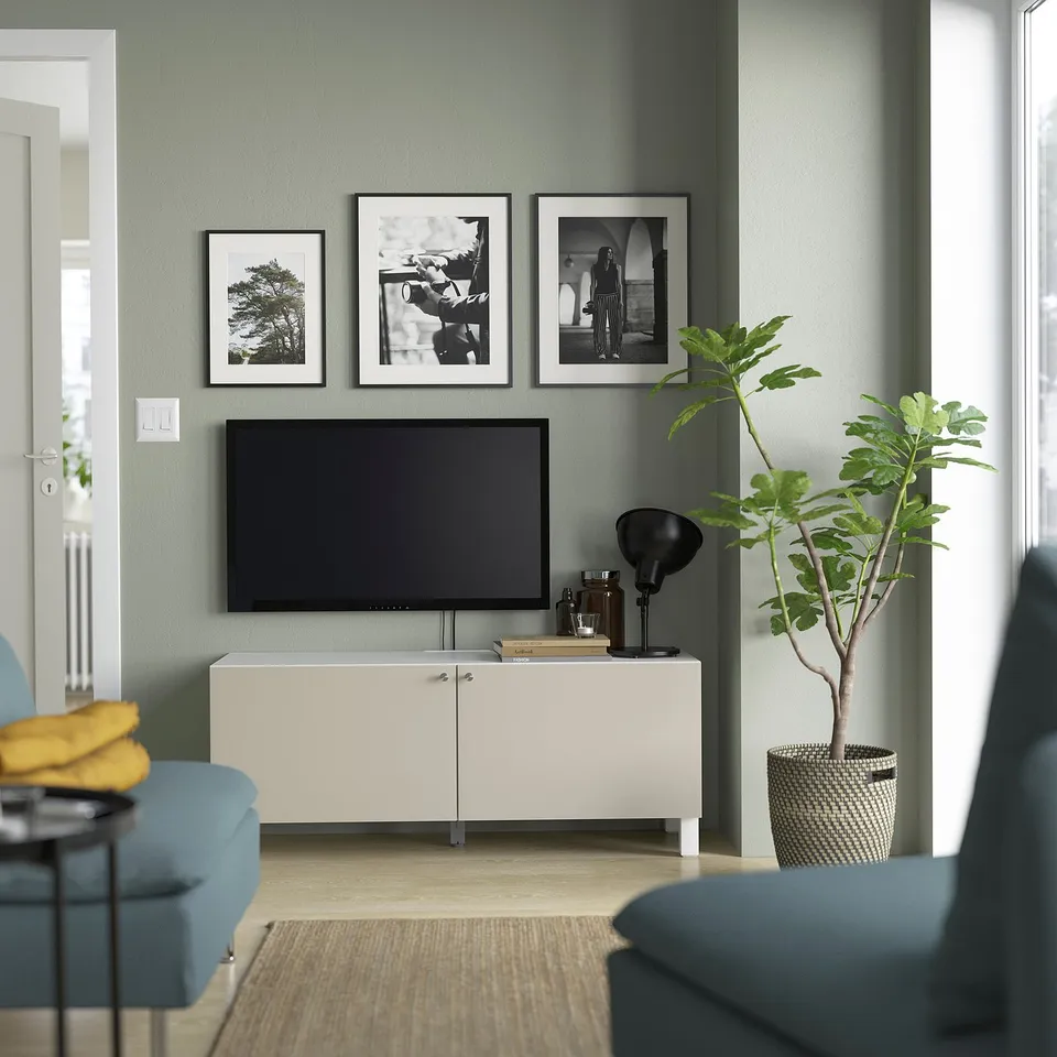 Modern living room with BESTÅ tv bench, blue sofa, flat screen tv, black lamp, and green plant. Light green wall, cosy seating.