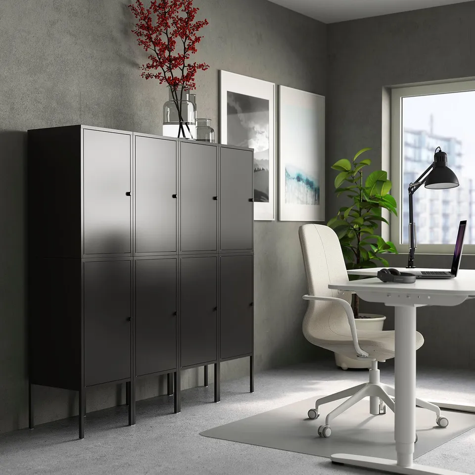 Modern office black LIXHULT storage cabinets, sleek desk with chair, colourful painting, and a laptop.