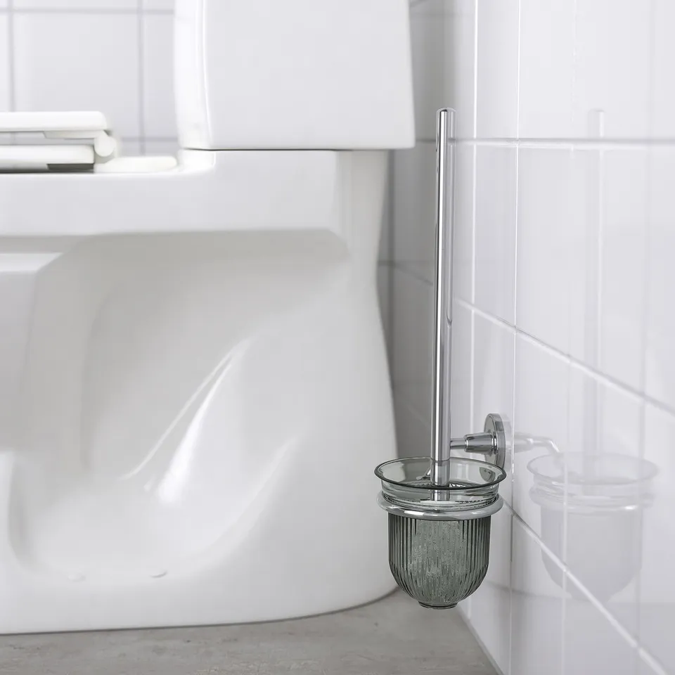 Toilet brush holder mounted on tiled wall, with brush and holder featuring shiny chrome details.