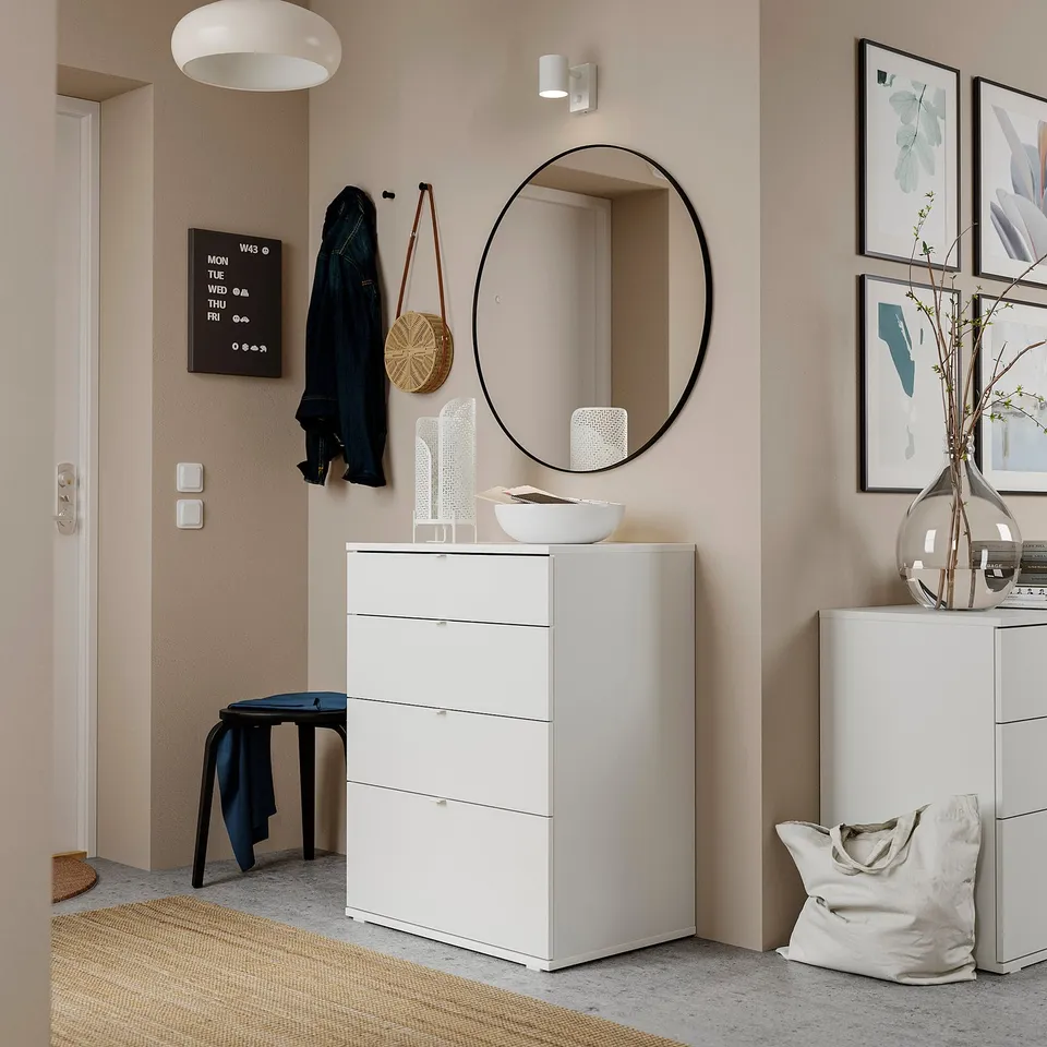 Modern entryway with white VIHALS chest, round mirror, wall hooks, and framed art.