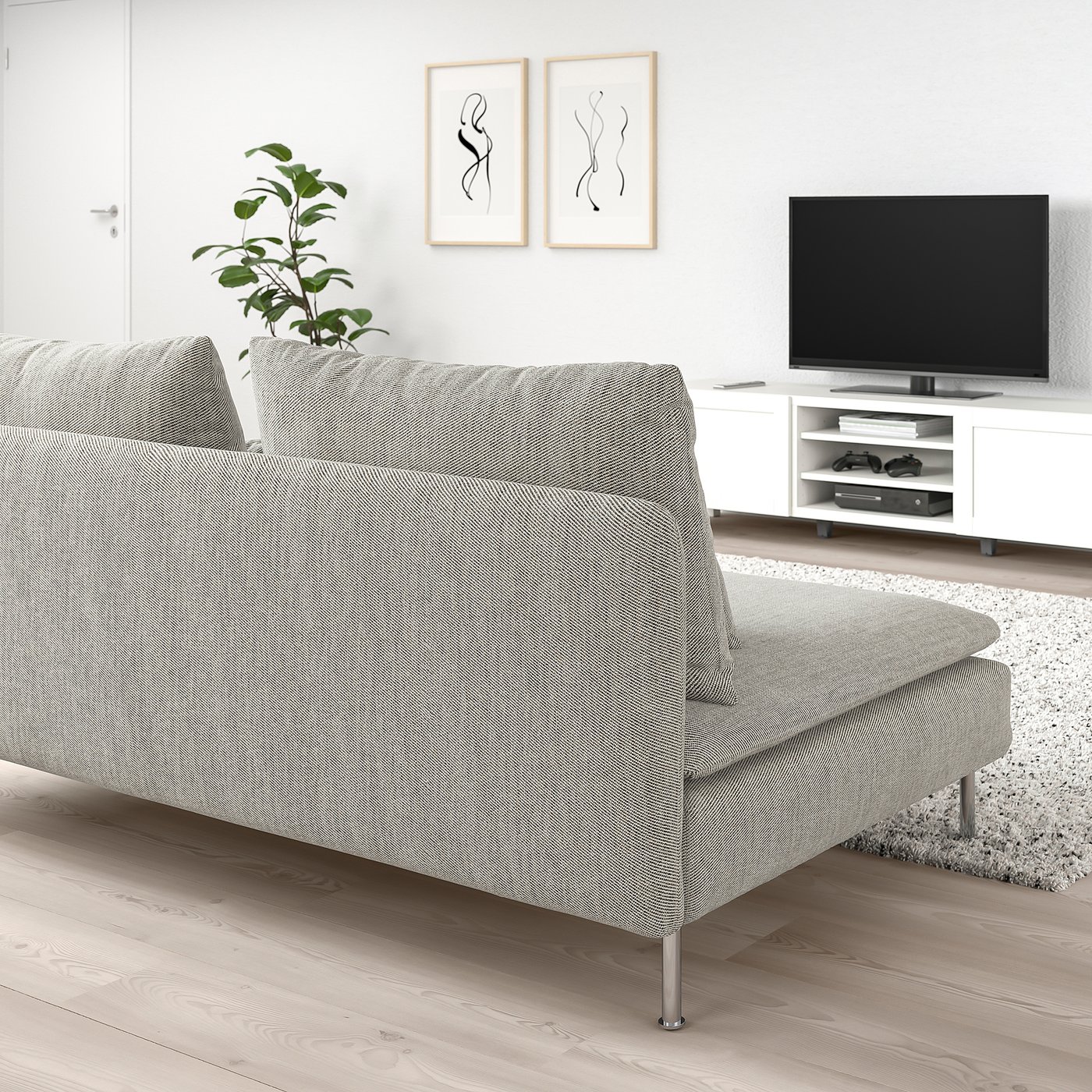 SÖDERHAMN sofa in light grey with loose cushions. Beside it, a white tv unit with gaming consoles. Minimalist room decor includes plant, art, and rug.