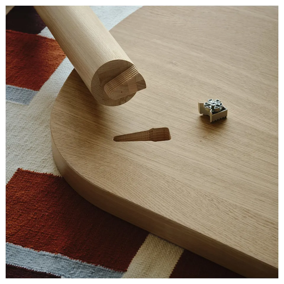 A wooden dining table with an assembly component and a metal spring joint on a colourful rug.