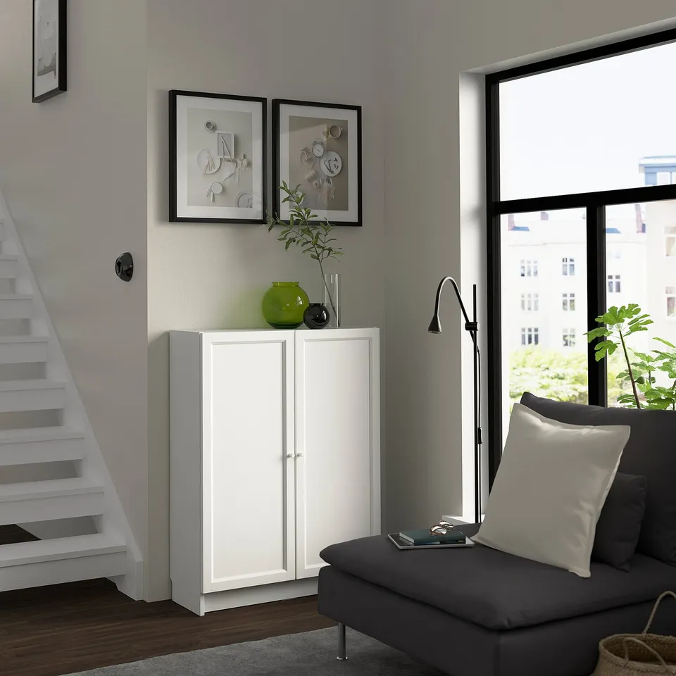 Modern living room with BILLY white cabinet, grey sofa, large window, green vase, and abstract wall art.