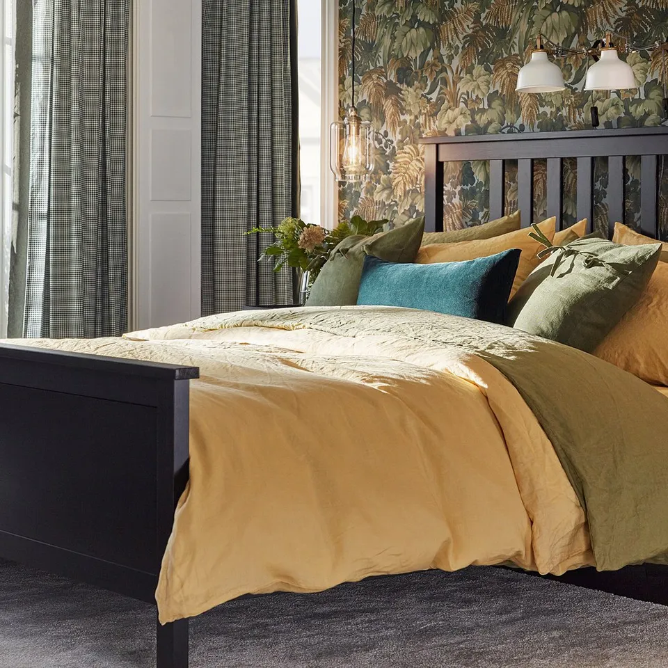 Bedroom with large bed, brown bedding, black headboard, green pillows, matching lamps, and dark green patterned wallpaper.