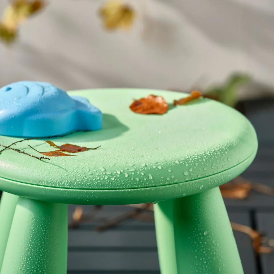 Small green kids table with water droplets, red leaves, and blue toy. Perfect for outdoor play and easy to clean.