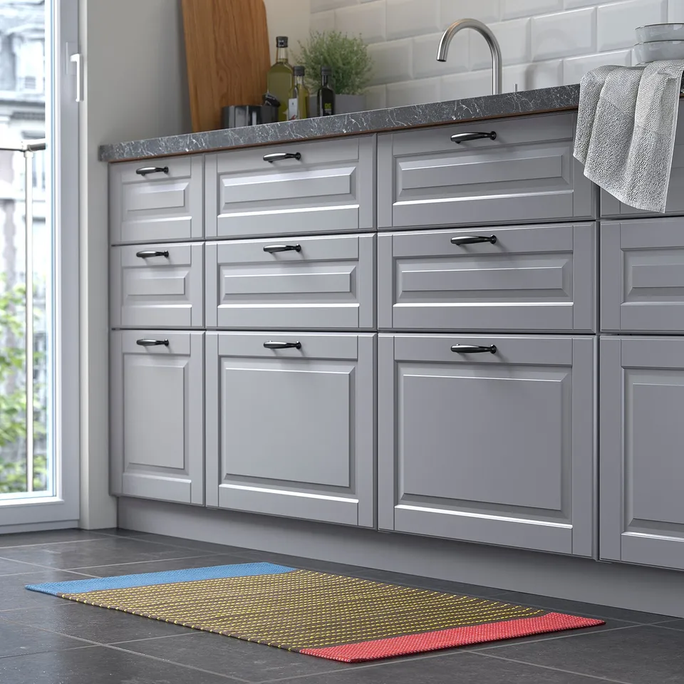 Modern kitchen with grey cabinets, marble counter, and colourful striped yellow, blue, red rug.