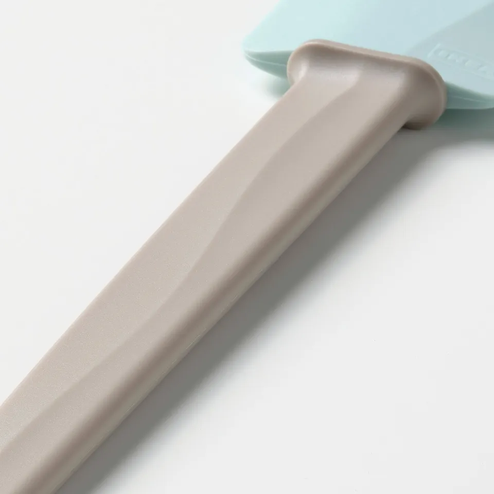 A mint green silicone spatula with a beige ergonomic handle on a white surface.