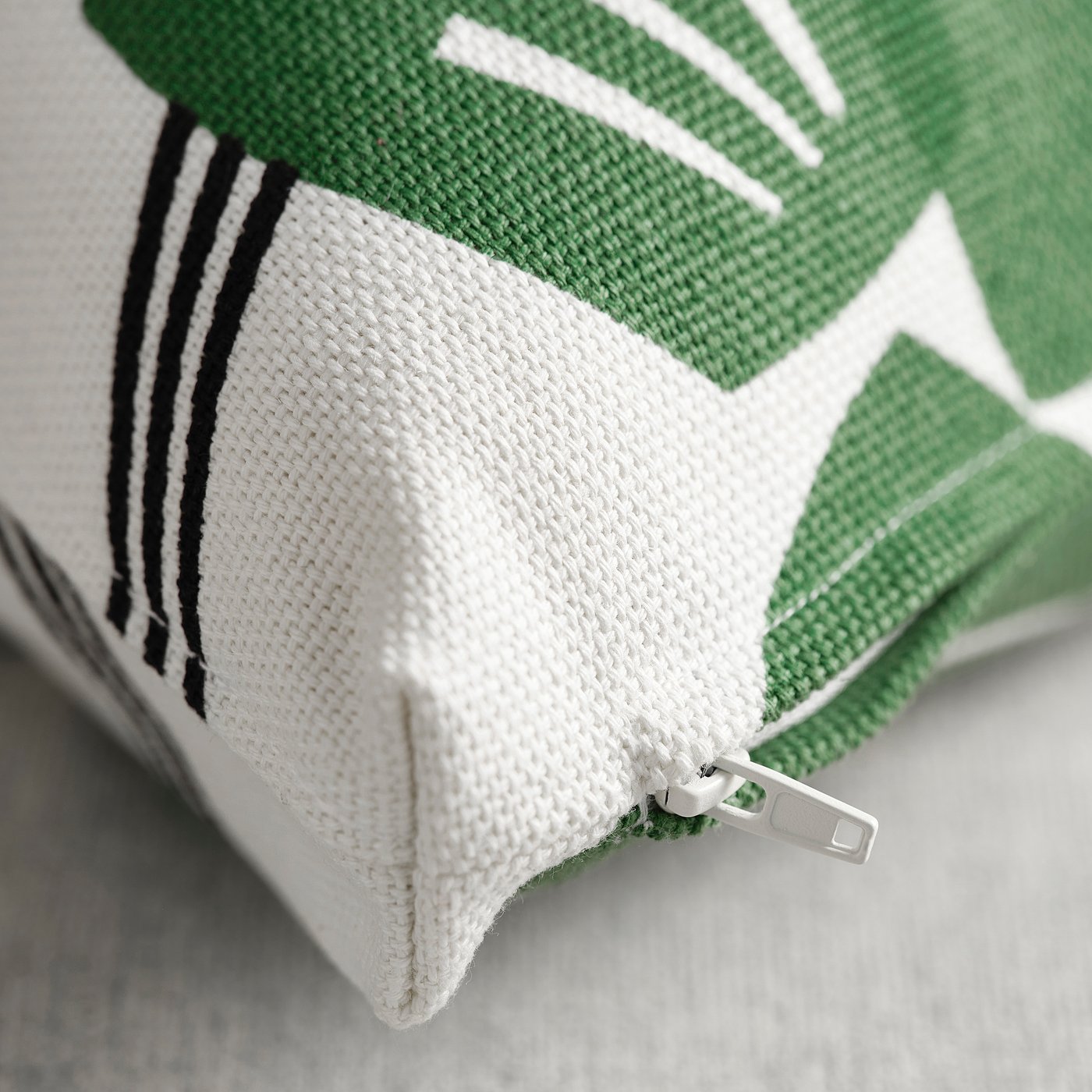Close-up of a square cushion cover with a zip, showcasing green leaf patterns on a white background, made of cotton and jute.