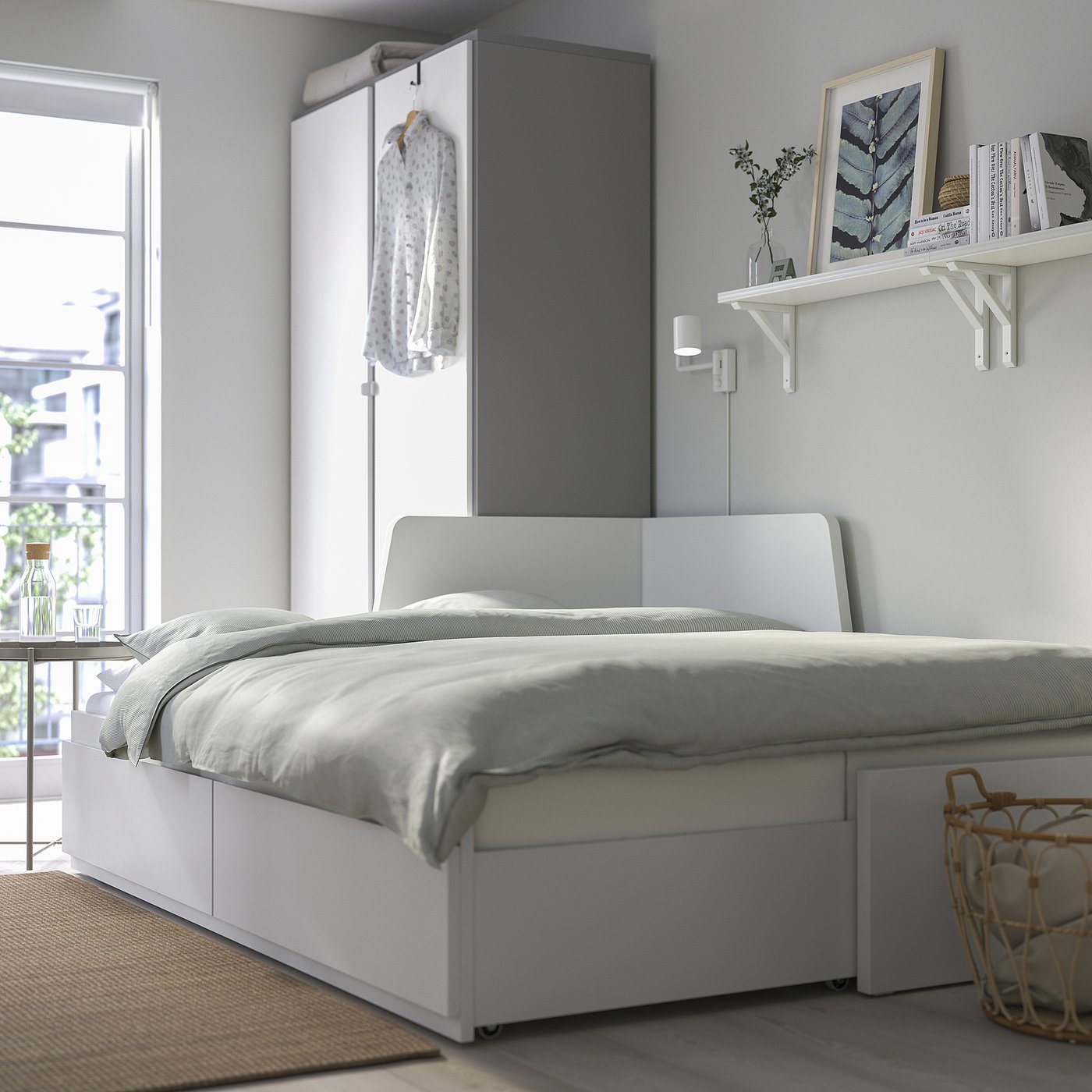 Minimalist bedroom with FLEKKE sofa-bed, featuring storage drawers, shelves with decor, and natural light from a window.