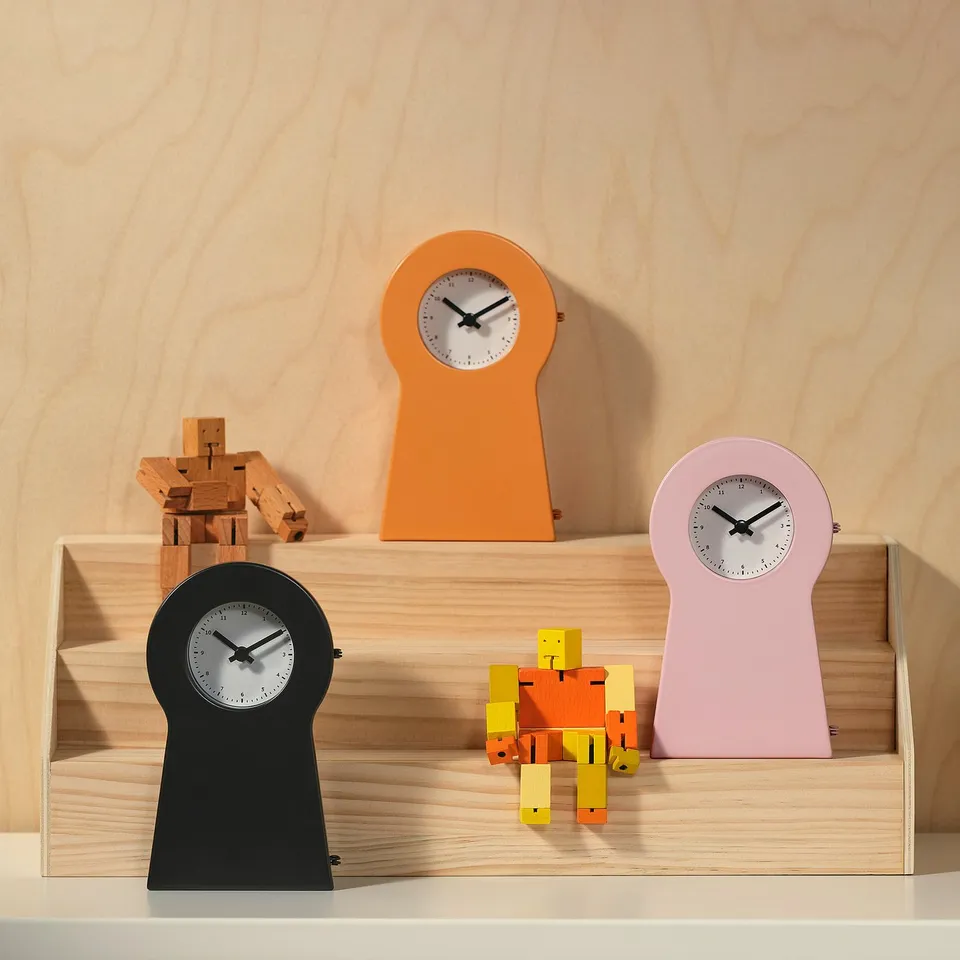 Three IKEA PS 1995 clocks with wooden robot toys on a light shelf.