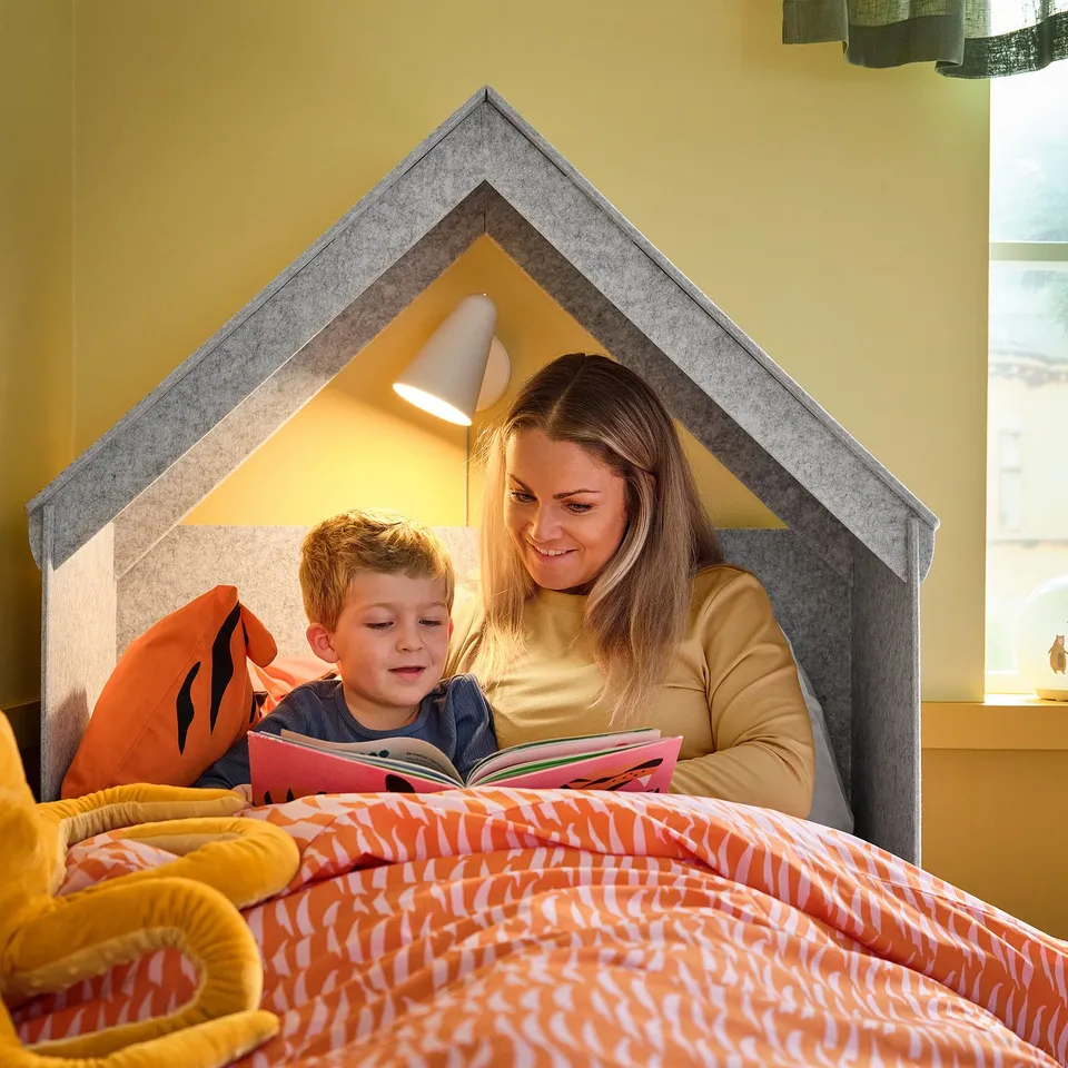 A person reads to a child in a cosy bed nook with a built-in lamp.