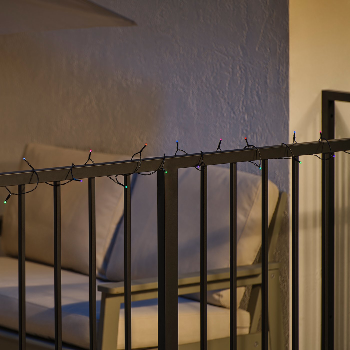 String lights on balcony railing, casting colourful glow on patio furniture.