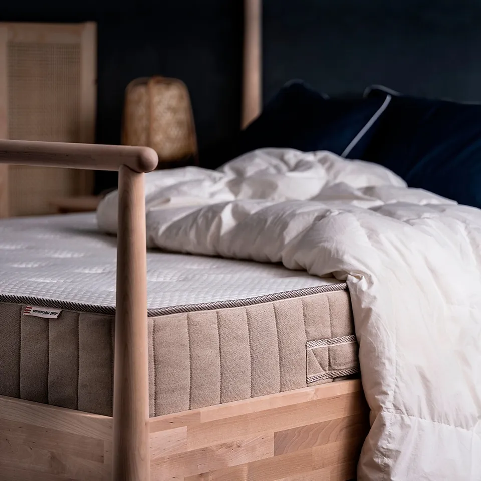 Bed with white mattress, dark pillows, wooden frame.
