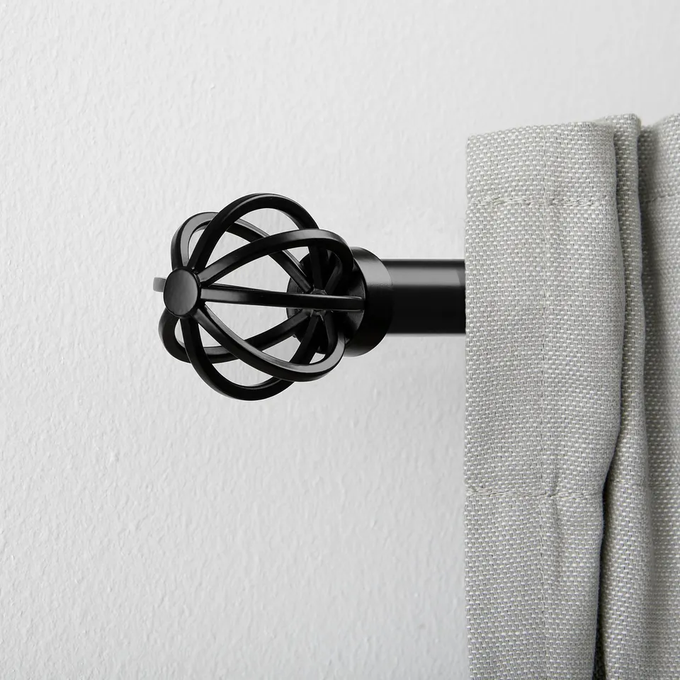 Black metal curtain finial in intricate spherical design, securely holding a grey curtain rod. Part of a decorative curtain set.