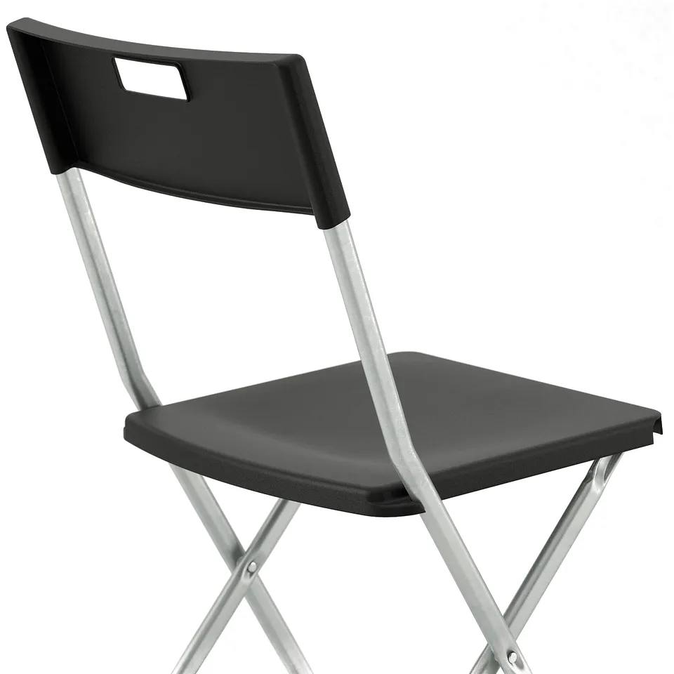 Black foldable chair with metal frame, square seat, and curved backrest against a white wall.