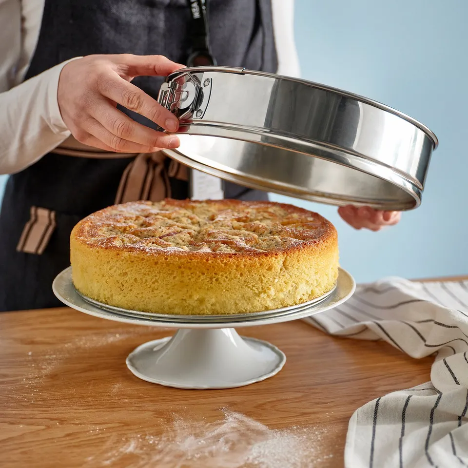 A person is removing a baked cake from a stainless steel springform pan, showcasing even baking and easy release.