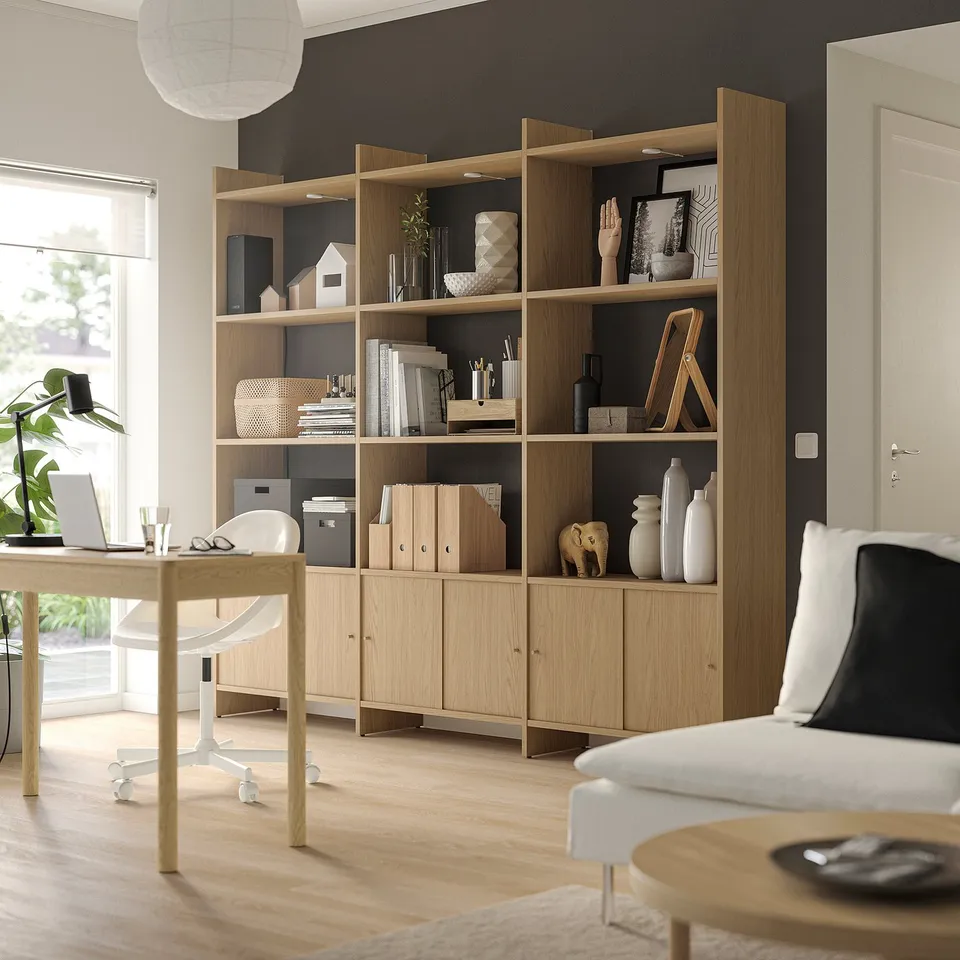 Modern workspace with light wood & black accents. Includes a large bookshelf, desk, and chair. Sleek design with decorative items and natural light.