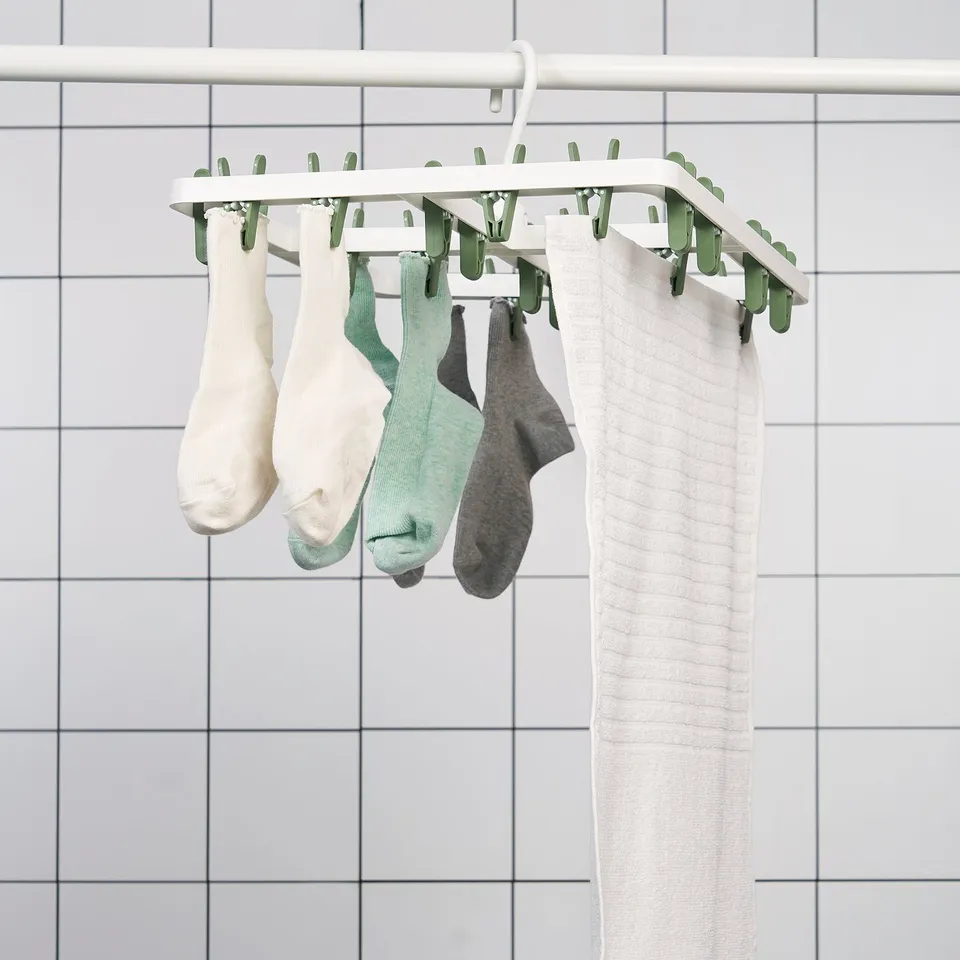 A drying rack hangs socks and underwear with clips against a tiled wall.
