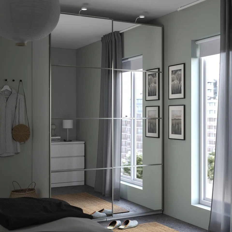 Modern bedroom with light blue walls, large mirror wardrobe, sliding doors, rattan rug, and framed photos.